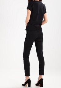 Svart kortärmad t-shirt i kombination med svarta skinny jeans och svarta högklackade skor, sedd bakifrån mot en enkel bakgrund.