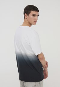 T-shirt in cotone con un design in gradiente da bianco a blu navy, maniche corte, vestibilità rilassata e scollatura rotonda. Vista posteriore mostrata.