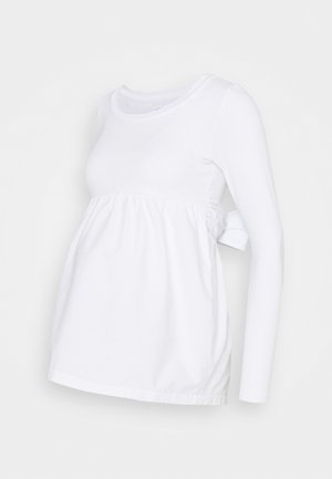 Blusa de maternidad blanca de manga larga en suave algodón, con un cuerpo fruncido, escote redondo y un lazo lateral para un ajuste relajado.