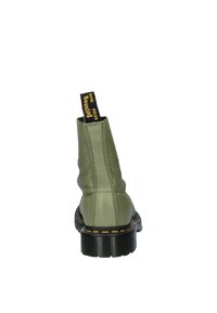 Botín de cuero verde con suela de goma negra, costuras amarillas y una lengüeta negra etiquetada "Bouncing Soles". Textura suave, diseño moderno.