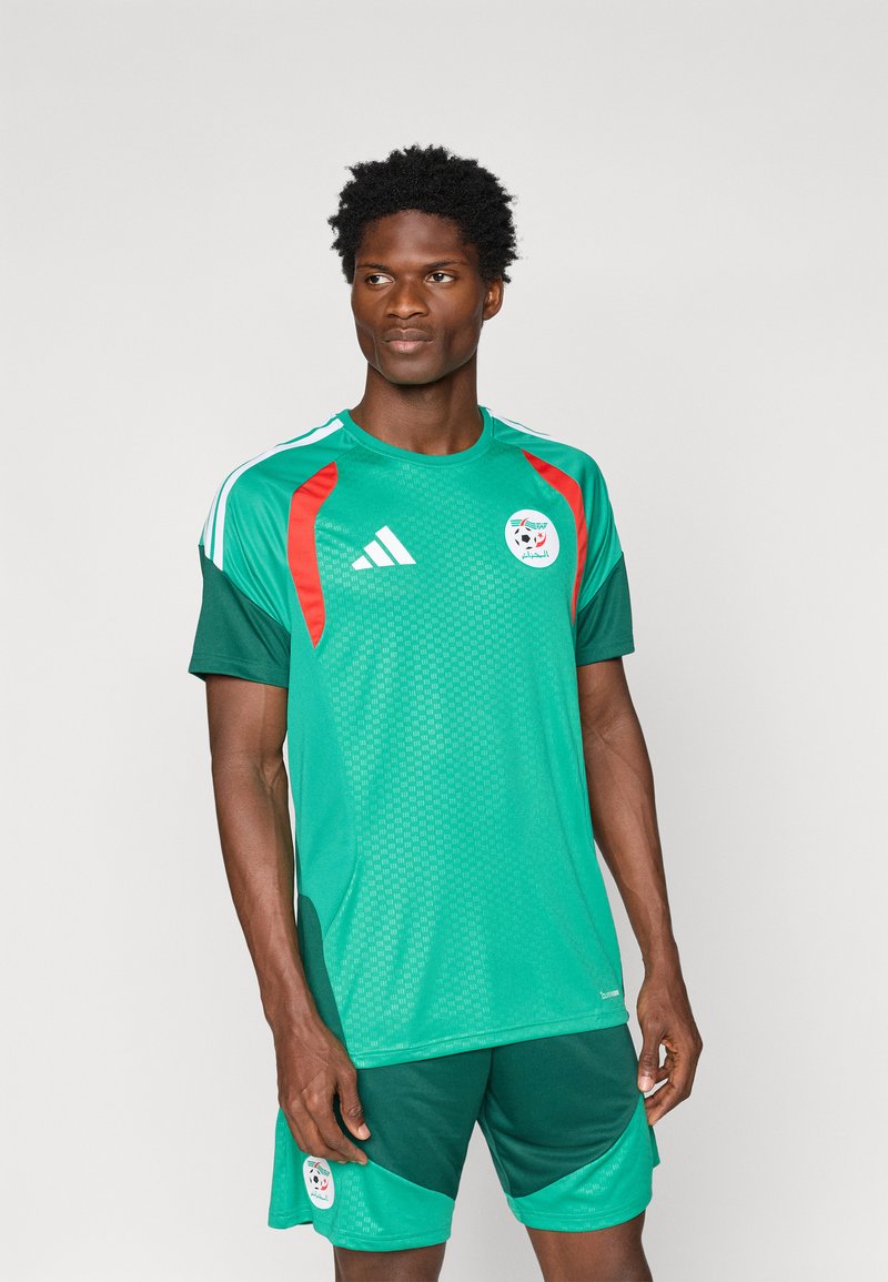 Camisa de futebol verde da Adidas com detalhes em vermelho e logótipo da equipa, acompanhada de calções verdes iguais. Textura em malha para respirabilidade.