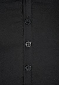 Gros plan sur un tissu noir avec une rangée verticale de trois boutons noirs, dont deux étiquetés "minimum" sur les bords.
