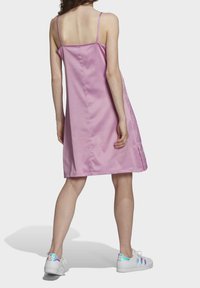 Różowa satynowa sukienka bez rękawów o prostym kroju, z gładką teksturą i szwem z tyłu. Zestawiona z białymi trampkami z iryzującymi akcentami.