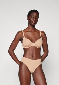 Beige seamless bra with molded cups and adjustable straps, paired with high-waisted bikini in matching color, smooth texture, and minimalist design.