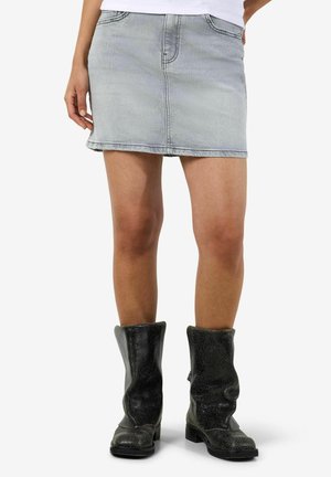 Persona che indossa una minigonna di jeans grigio chiaro e stivali neri con texture fino a metà polpaccio, in piedi con le gambe leggermente divaricate.