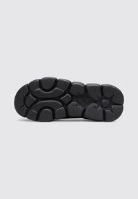 Suela de sneaker negra con agarre de goma texturizada, que presenta un patrón de secciones elevadas variadas para tracción y durabilidad.