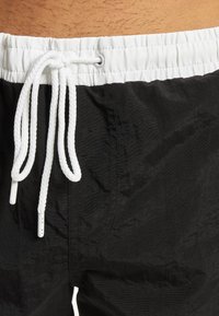 Mustat uimapuvut tekstuurilla, joissa on valkoinen nyöri joustava vyötärö ja huomaamattomat tikkaus yksityiskohdat.