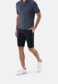 Námořnické polo tričko s tříknoflíkovou légou, doplněné o tmavé šortky. Bílé tenisky s texturovanou podrážkou. Hladká textura látky po celém povrchu.