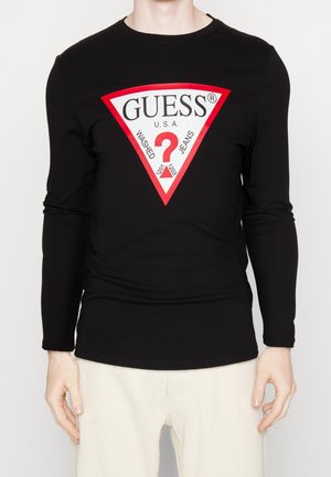 Czarna koszula z długim rękawem z dużym czerwono-białym trójkątnym logo Guess z znakiem zapytania i napisem "Washed Jeans" na piersi.