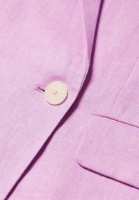 Liliowy żakiet z gładkiego materiału, z pojedynczym okrągłym guzikiem i kieszenią, podkreślający dopasowany fason.