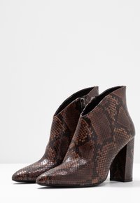 Brązowe botki za kostkę w wzór imitujący skórę węża, z noskiem w szpic, teksturowaną powierzchnią i masywnym obcasem. Wyposażone w boczny zamek błyskawiczny dla łatwości zakładania.