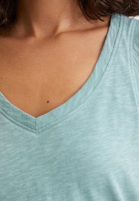 Jasnoniebieska bluzka typu v-neck z miękkiego, teksturowanego materiału. Charakteryzuje się prostym designem z czystym dekoltem i brakiem wyraźnych wzorów lub akcentów.