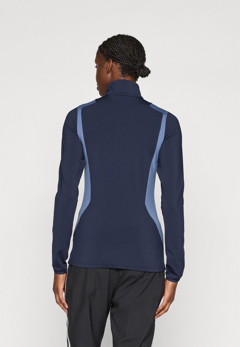 Haut à manches longues bleu marine avec un col haut, présentant des panneaux latéraux bleu clair, un design ajusté et une texture lisse. Idéal pour les vêtements de sport.