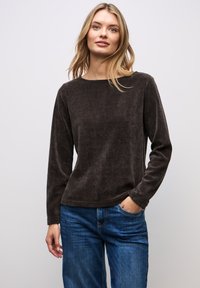 Camicia marrone a maniche lunghe in tessuto texturizzato con scollo a barca. Abbinata a jeans di denim blu, con una vestibilità rilassata e tasche.