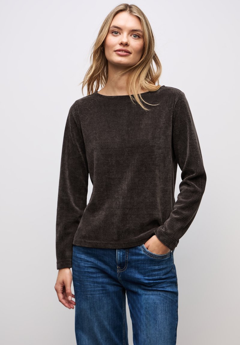 Camicia marrone a maniche lunghe in tessuto texturizzato con scollo a barca. Abbinata a jeans di denim blu, con una vestibilità rilassata e tasche.