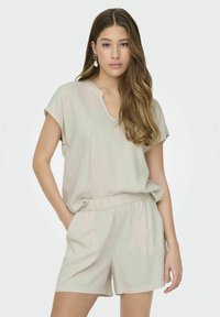 Jasno beżowy strój składający się z krótkiego topu z dekoltem w serek oraz szortów z elastycznym pasem. Miękka, teksturowana tkanina o luźnym kroju.