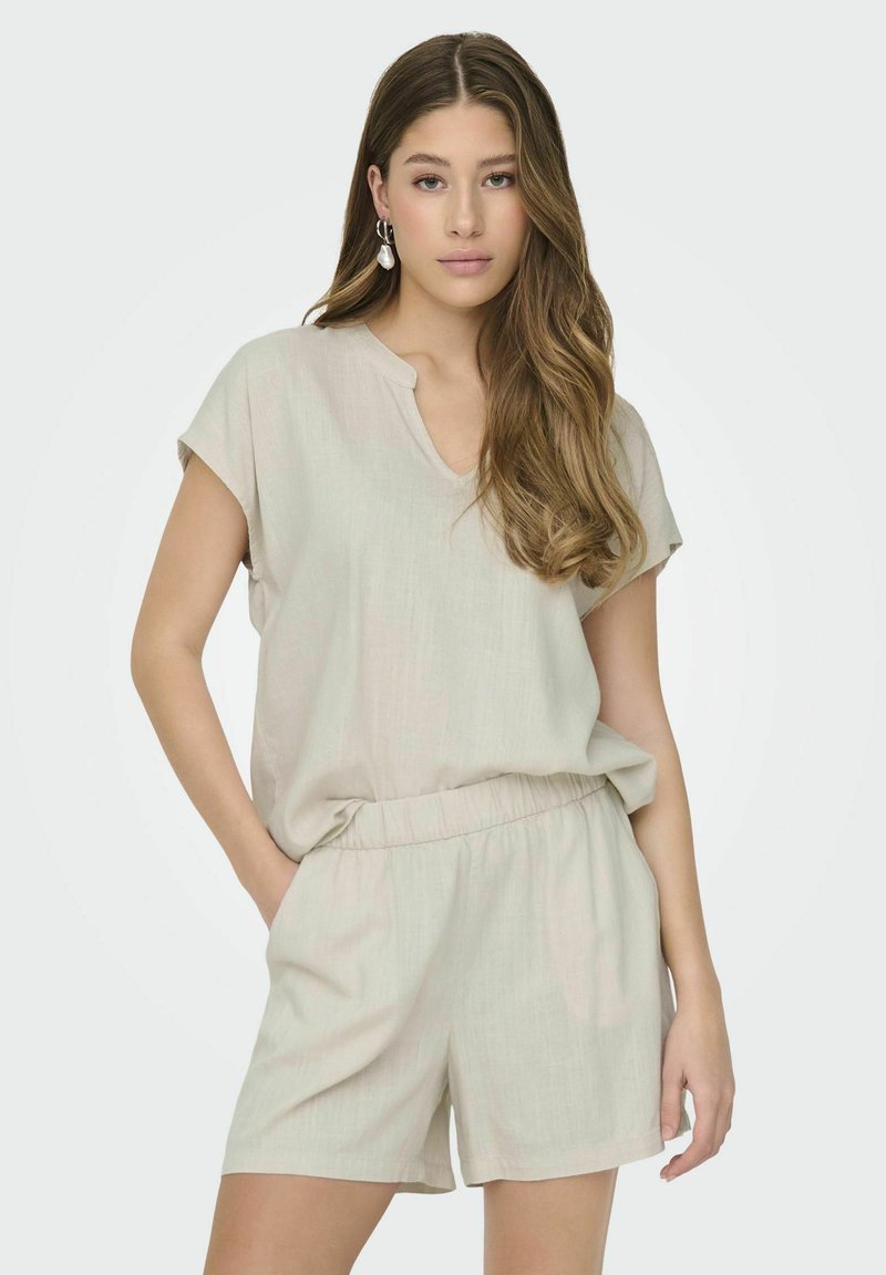 Jasno beżowy strój składający się z krótkiego topu z dekoltem w serek oraz szortów z elastycznym pasem. Miękka, teksturowana tkanina o luźnym kroju.