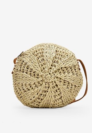 Rund beige vævet stråtaske med radialt mønster og en tynd brun læder skulderrem på hvid baggrund.