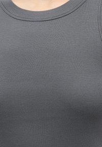 Gros plan d'un haut sans manches côtelé gris montrant la texture du tissu et un col rond sur une peau claire.