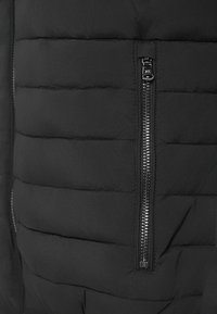 Secção de casaco acolchoado preto com quilt horizontal, um bolso com fecho éclair metálico e uma textura de tecido suave.