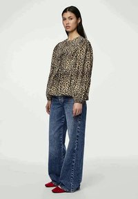 Μπλούζα με λεοπάρ σχέδιο και μαζεμένη μέση, μπαλόνι μανίκια, συνδυασμένη με φαρδιά μπλε τζιν και κόκκινα σουέτ παπούτσια.