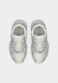 Ανοιχτό γκρι πλεκτά αθλητικά παπούτσια με υφασμάτινες επικαλύψεις, λευκά κορδόνια και μαλακή σόλα, με κομψό σχεδιασμό και λογότυπο στη γλώσσα.