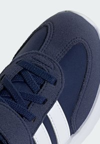 Baskets de sport bleu marine avec une combinaison de tissu texturé et de maille lisse, ornées de rayures blanches et de lacets assortis.