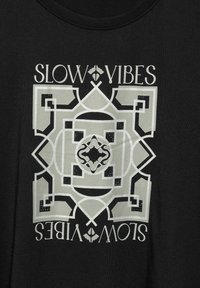 Černé tričko s velkým centrálním geometrickým vzorem v světle šedé barvě, s nápisem "SLOW VIBES" nahoře a dole.