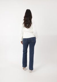 Hvid strikket sweater med ribbet kant og struktureret detaljer, parret med mørkeblå flagrende jeans og gennemsigtige blokhælede sko.