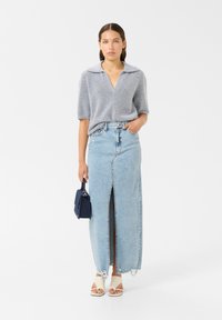 Siva kratka majica s kratkimi rokavi in ovratnikom, v kombinaciji z svetlo modrim jeans krilom z sprednjim razporkom in strganim robom. Bele natikače in mornarsko modra torba.