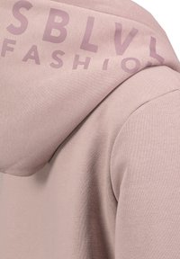 Light pink hoodie with a smooth texture, featuring large, purple lettering on the shoulder spelling "FASHION." Simple design, casual fit.