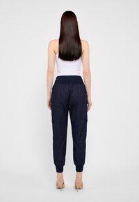 Pantalones cargo azul marino con cintura elástica y puños en los tobillos, que cuentan con dos bolsillos laterales y una tela suave y texturizada, llevados con una blusa blanca.