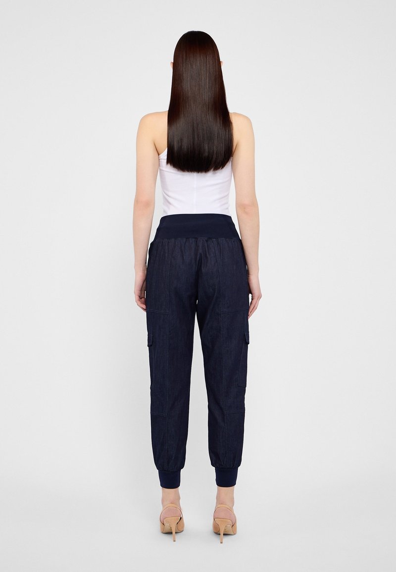 Pantalones cargo azul marino con cintura elástica y puños en los tobillos, que cuentan con dos bolsillos laterales y una tela suave y texturizada, llevados con una blusa blanca.