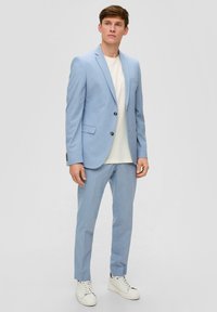 Giacca e pantaloni di colore azzurro chiaro, realizzati in tessuto liscio, con un taglio su misura, chiusura con un bottone singolo e una t-shirt bianca sotto.
