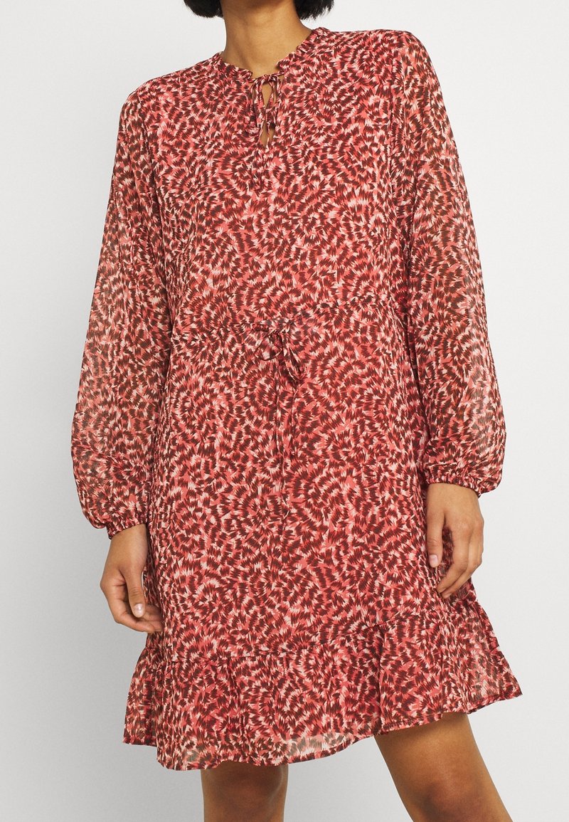 Červeno-bílá vzorovaná šaty s výstřihem ve tvaru klíčové dírky, dlouhými rukávy a nařaseným pasem, s volánkovým lemem a průsvitnou texturou.