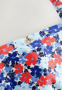 Tissu fleuri avec des fleurs rouges, bleues et bleu marine et une petite fermeture circulaire dorée avec une ligne diagonale au centre.