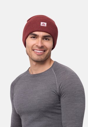 Maroon knit beanie with a folded brim, featuring a small white logo patch. Model wears a gray long-sleeve shirt, displaying a snug fit.
