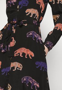 Svart klänning med ett djärvt mönster av orange, lila och rosa leoparder. Mjuk tyg, knappdetaljer och ett knytbart midjebälte.