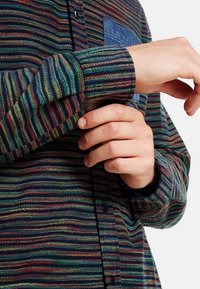 Randig skjorta i flera färger gjord av vävt material med långa ärmar, en ficka i blå denim och knappar fram.