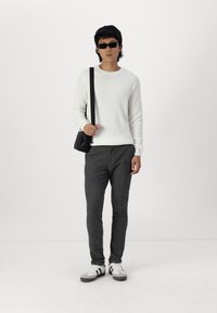 Suéter blanco con relieve, pantalones oscuros grises ajustados, bolso negro de hombro, gafas de sol negras y zapatillas grises con acentos en blanco y negro.