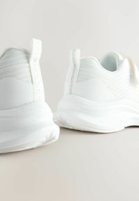 Baskets blanches de sport avec une tige en tissu texturé, semelle en caoutchouc lisse et détails de couture discrets. Présentent un design flexible et un col rembourré.