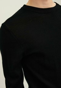 Chemise noire à manches longues avec encolure ronde et poignets côtelés. Tissu tricoté à la texture lisse, présentant une coupe ajustée.