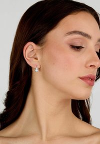 Orecchini a goccia con una pietra blu chiaro, montati in metallo tono argento, caratterizzati da un design elegante e da una leggera lucentezza sulla pelle.