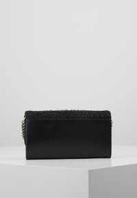 Borsa nera con base in pelle liscia e parte superiore in tessuto morbido e testurizzato. Presenta un accento in catena argentata su un lato. Forma rettangolare.