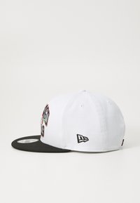 Fehér baseball sapka fekete árnyékkal, színes hímzett szöveggel az elülső részén és logóval az oldalán. Az anyaga sima pamut.