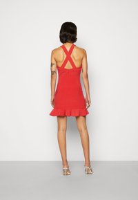 Vestido vermelho sem mangas com bainha evasê, alças cruzadas nas costas e fecho com zíper nas costas. Feito de um tecido liso e elástico.