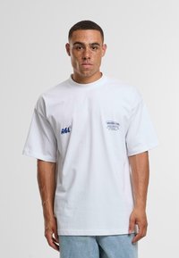 Camiseta de algodón blanca con corte holgado, cuello redondo acanalado, y detalles en texto azul: "ACL" y "ANOTHER CROP" en la parte frontal.