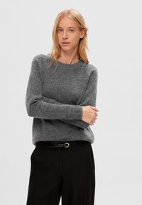 Grå strikket sweater med rund hals og lange ærmer, parret med sorte bukser, der har et slankt sort bælte med en guldspænde.