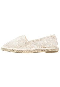 Espadrille en dentelle de couleur crème, avec un bout arrondi, une semelle intermédiaire en jute tissé et un motif floral en dentelle décoratif sur le haut.
