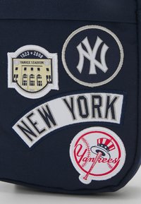 Tessuto blu con quattro toppe ricamate: una distintivo dello Yankee Stadium, un logo di NY, un banner "NEW YORK" e il logo dei Yankees di baseball con un cappello a cilindro.